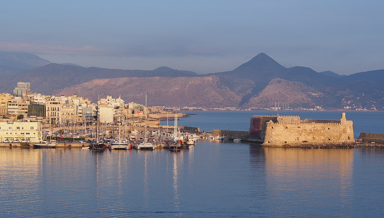 A stone sea fortress at the mouth of a calm harbour full of yachts, with the town and a pointed mountain behind.