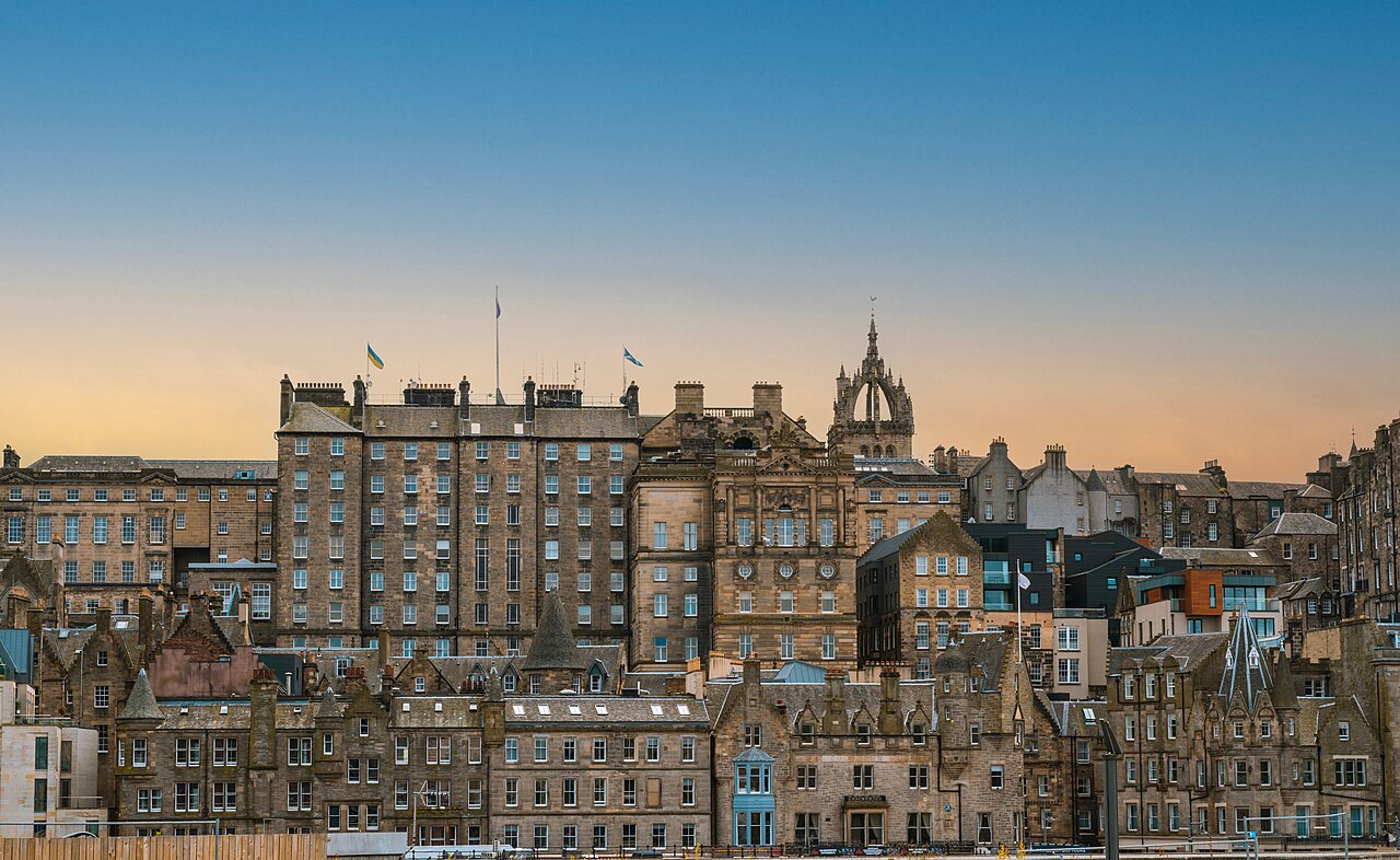Tall stone tenement buildings rising across the hillside below a clear sky at twilight.