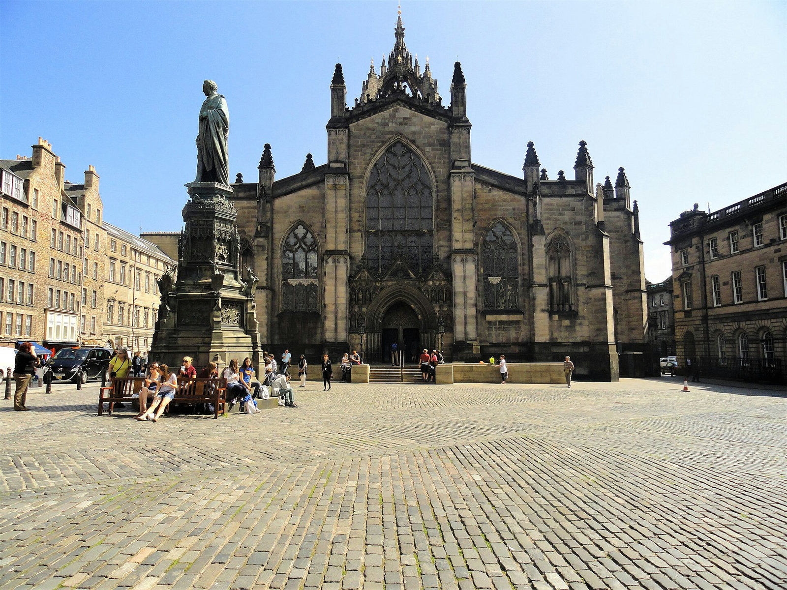 A wide view across a cobblestone square towards a historic stone cathedral under a clear blue sky.