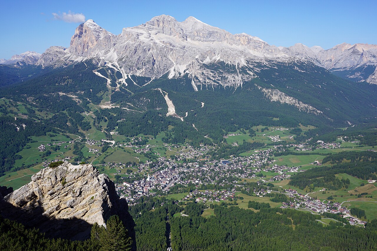 A town spreads across a green valley floor far below pale, jagged limestone peaks.