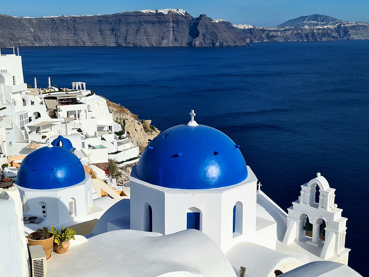 Two bright blue church domes and a white bell tower stand above whitewashed houses and a deep blue sea.