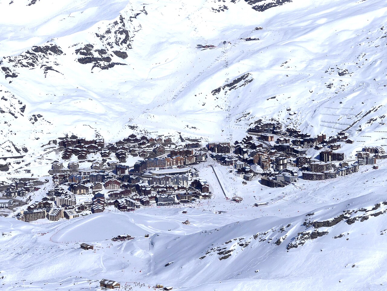 A dense cluster of chalet-style buildings in a bowl of snow-covered slopes, seen from above.