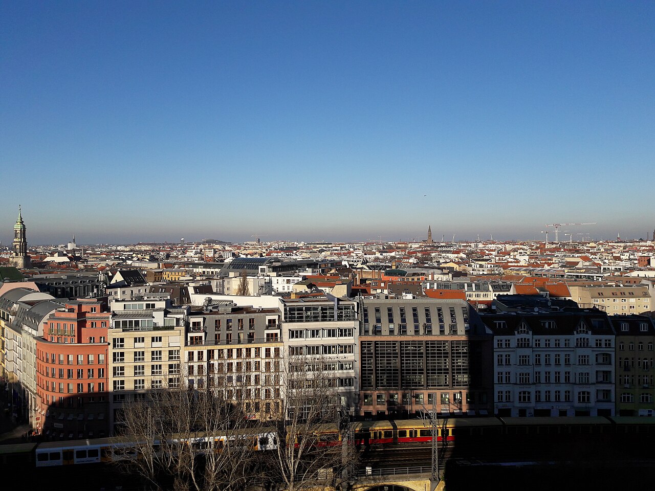 Rooftops of a city stretching to a flat horizon under a clear sky, with apartment blocks in the foreground.