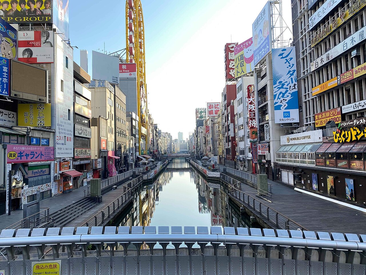 A straight canal with walkways on both sides, running between buildings covered in large signs.