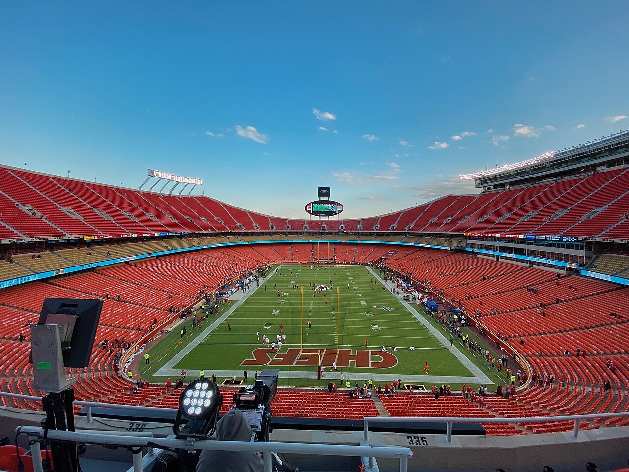 An empty stadium bowl with red seating around a green field, seen from high in the stands.