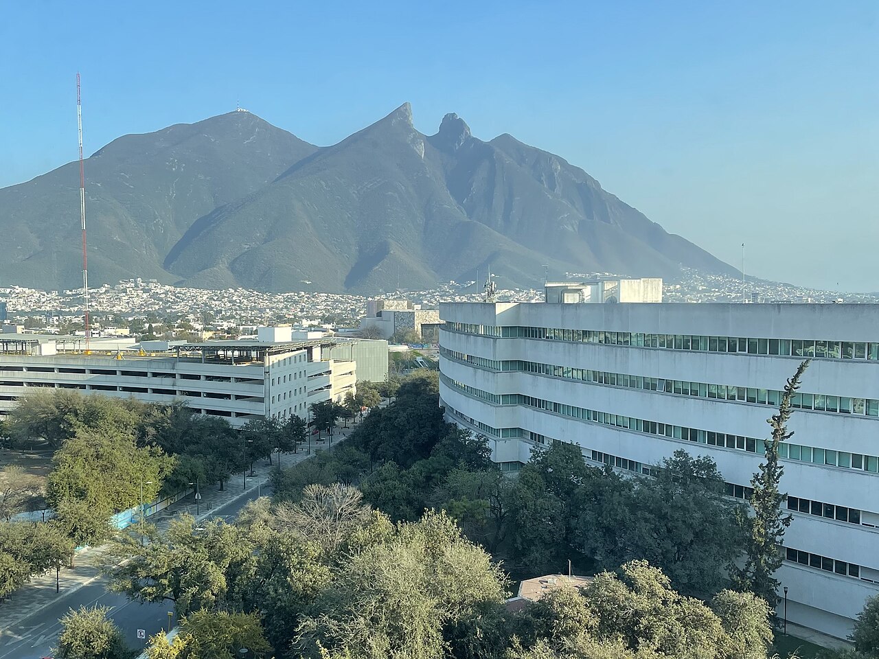 A saddle-shaped mountain against a clear sky, with long white campus buildings and trees in the foreground.