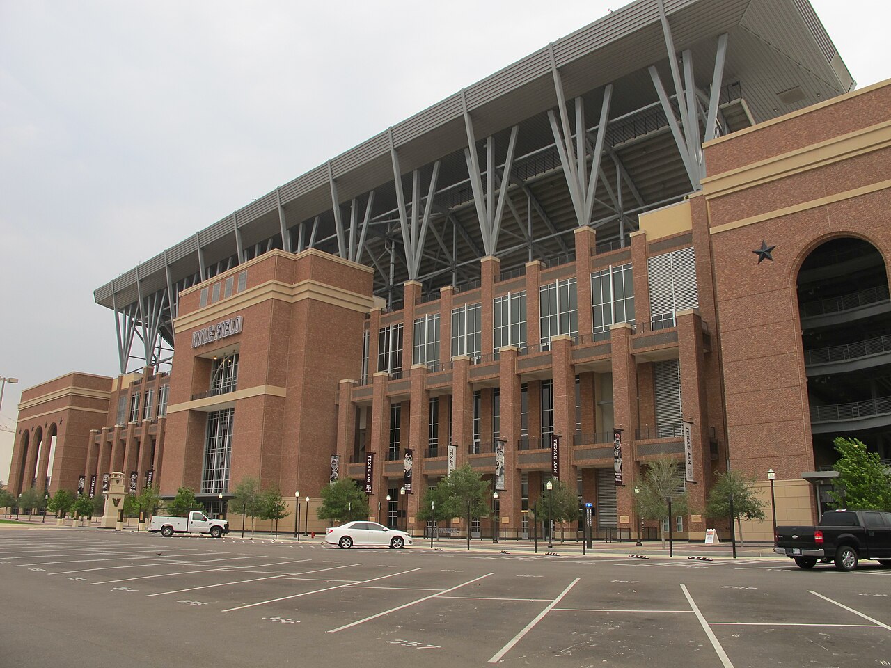 A very large brick and steel stadium seen from across an almost empty car park.
