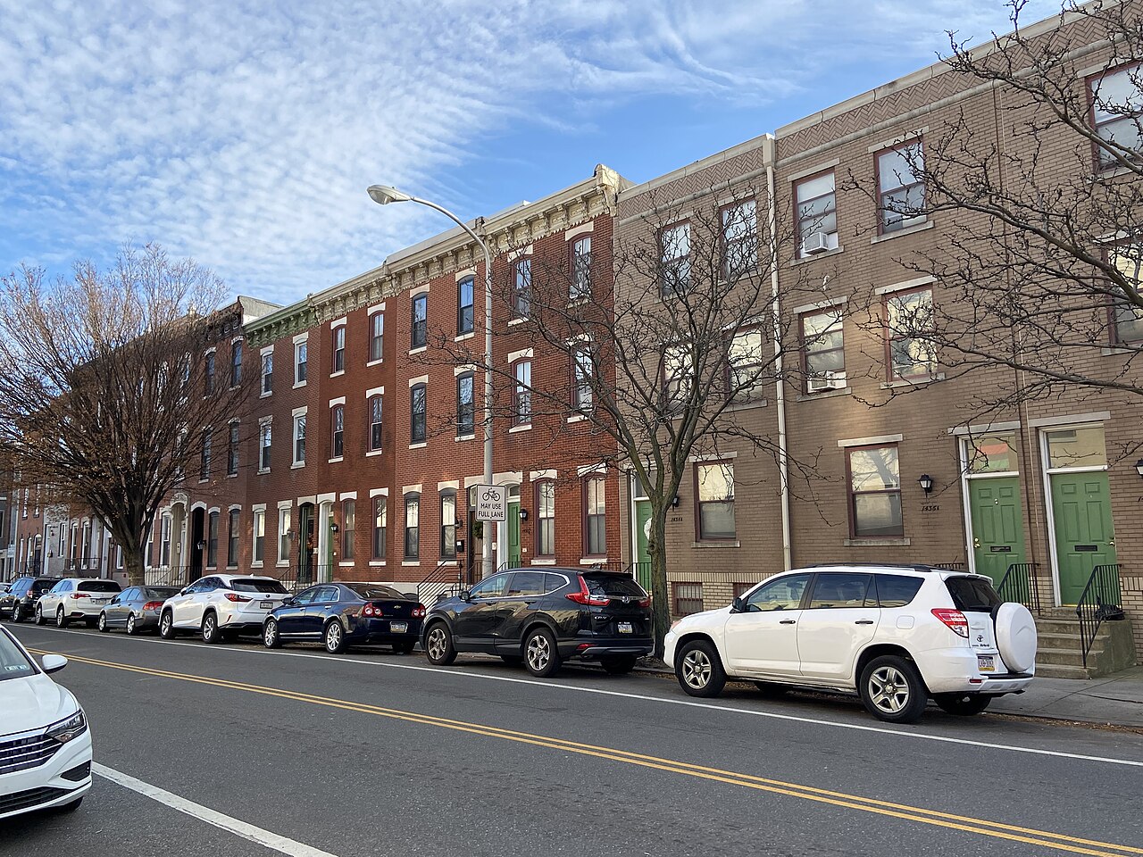 A terrace of three-storey brick row houses along a street with parked cars and bare winter trees.