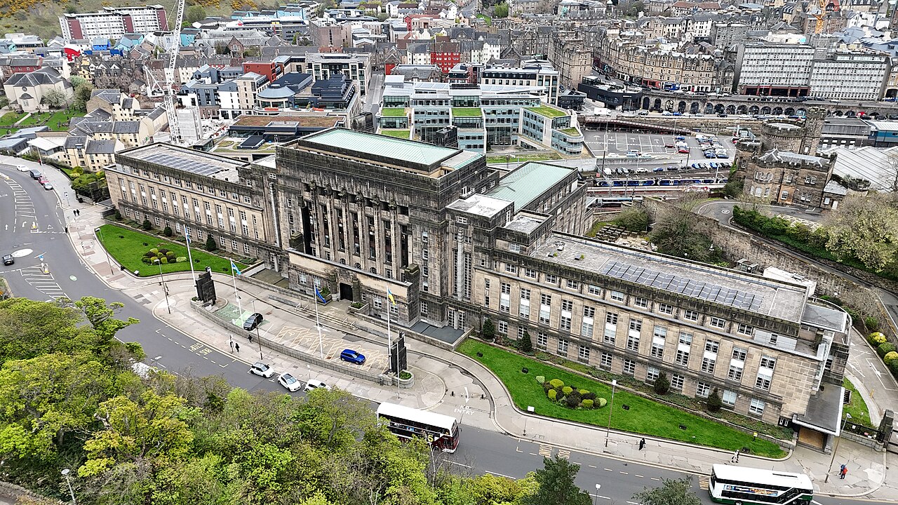 A large symmetrical stone office building on a hillside, seen from above with the city spread out behind it.