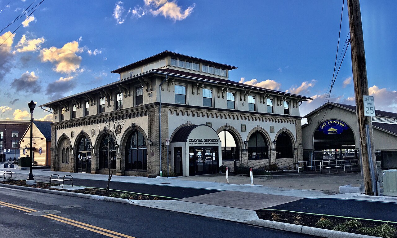 A two-storey cream building with arched ground-floor windows and a tiled roof on a street corner under a blue sky.