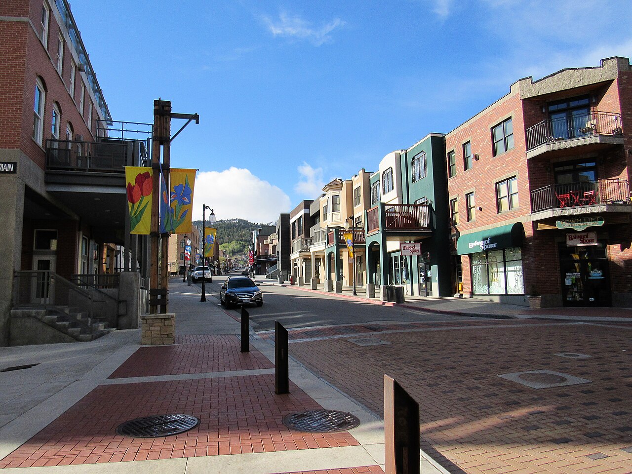 A sloping street lined with three-storey brick and painted shopfronts, with hills at the far end.