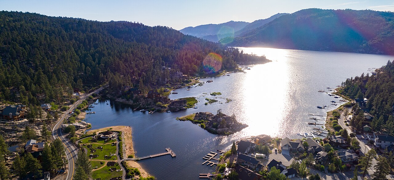 Sunlight glints off a mountain lake edged with boat docks, a road and forested slopes.